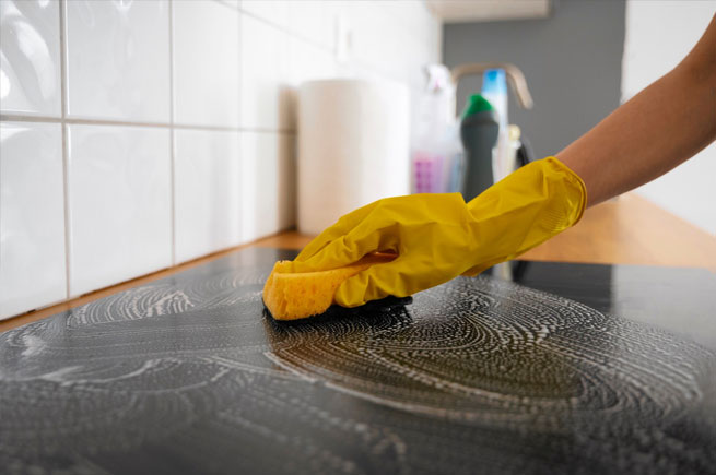 Person cleaning a glass stovetop with a sponge, ensuring it is spotless and free of grime.