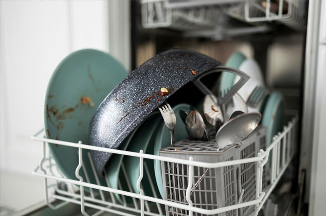 A dishwasher full of dirty dishes after a wash cycle, with food particles still visible on plates and utensils.