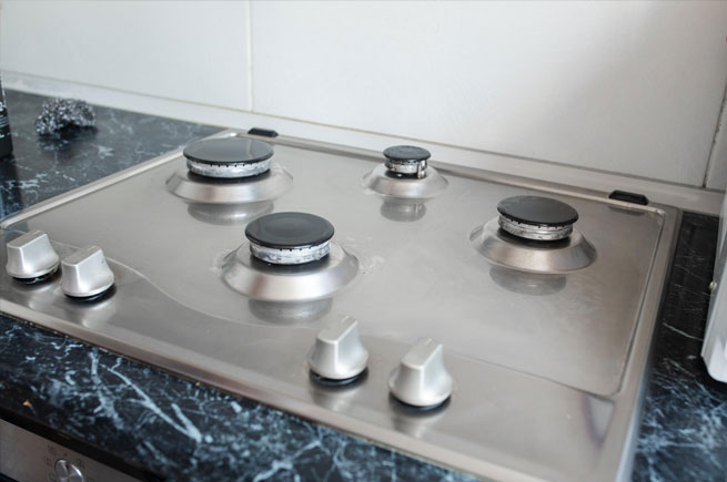 tainless steel gas stove with a sleek, minimalist design, featuring four burners on a black marble countertop.