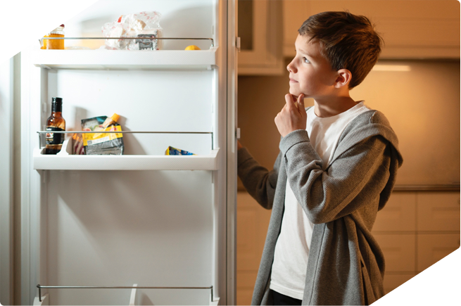 Boy thinking in front of an open refrigerator, pondering what to eat next from the fridge.