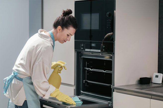 Woman cleaning an oven using natural cleaners to achieve a sparkling result without harsh chemicals.