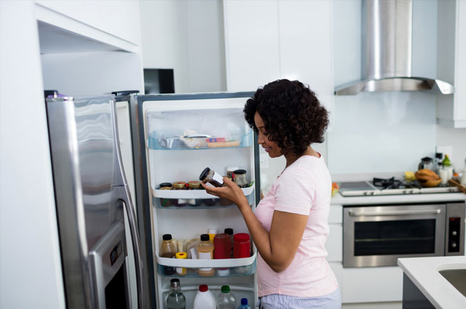 A woman organizing her refrigerator to ensure food stays fresh and neatly stored.